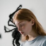 A woman looks anxious with a spider in the background, conveying fear and solitude.